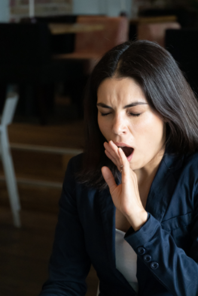 A tired professional woman yawning behind her hand in a quiet café
